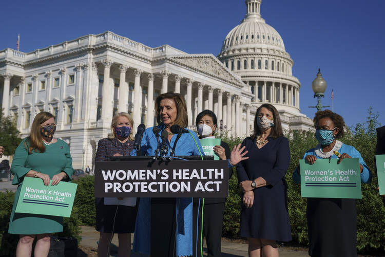 House Speaker Nancy Pelosi stands at a blue lectern with the U.S. Capitol in the background.