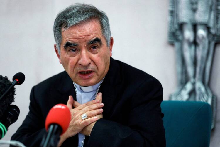 A man in priest's clothing speaks into a red microphone.