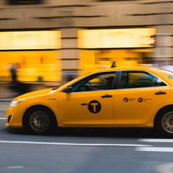 Stock image of a yellow taxi blurred as it speeds down the road.
